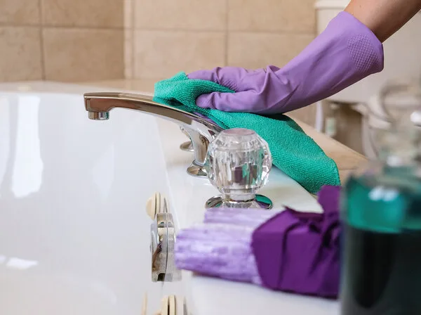 Purple-gloved hand wiping a chrome bathtub faucet with a green cloth