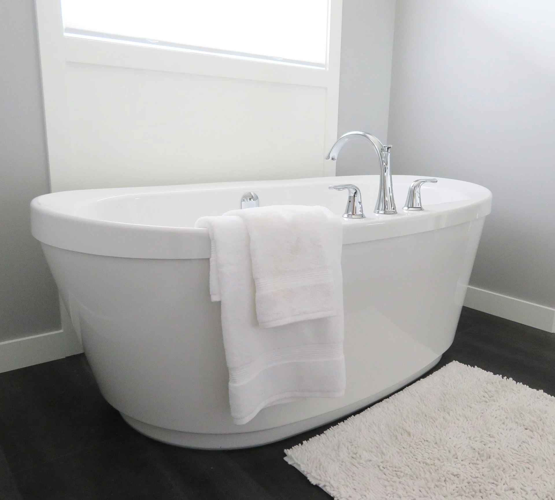 Clean white freestanding bathtub with towels, chrome fixtures, and a bath mat