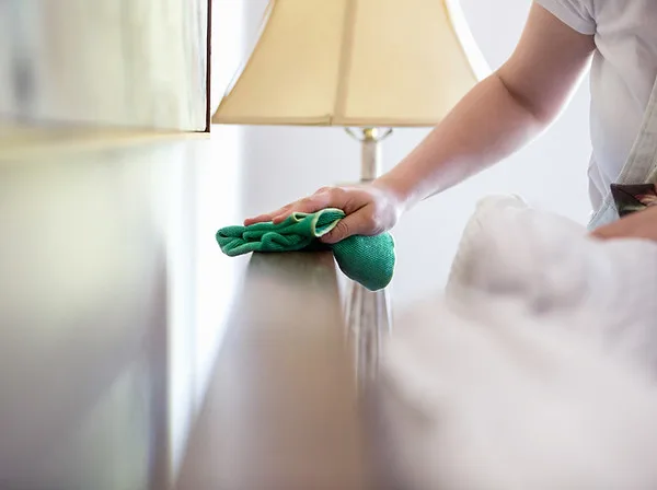 Person wiping a wooden furniture surface with a green cleaning cloth